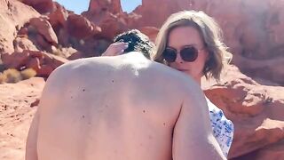 A wife is having fun with her friend in front of her husband in the desert