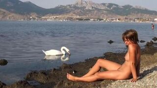A girl is completely naked on the riverbank and sunbathes